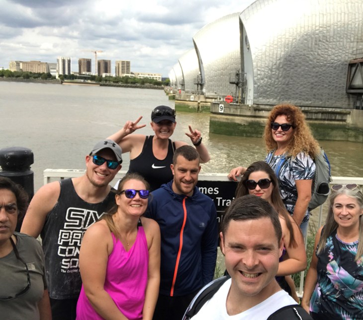 Mixed group of fundraisers standing by the Thames River, giving thumbs up