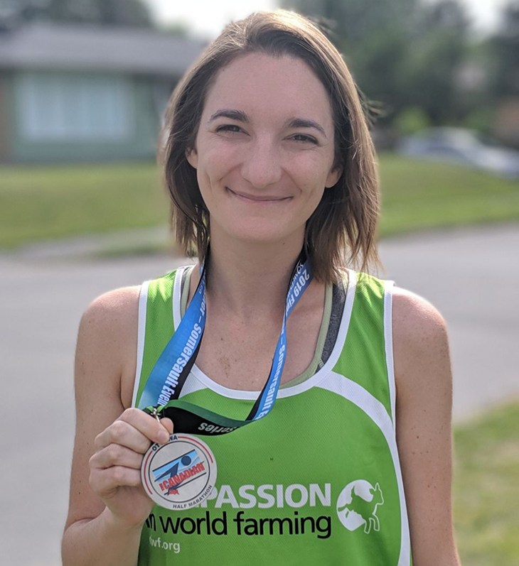 Female runner proudly holding her medal wearing a CIWF UK green running vest